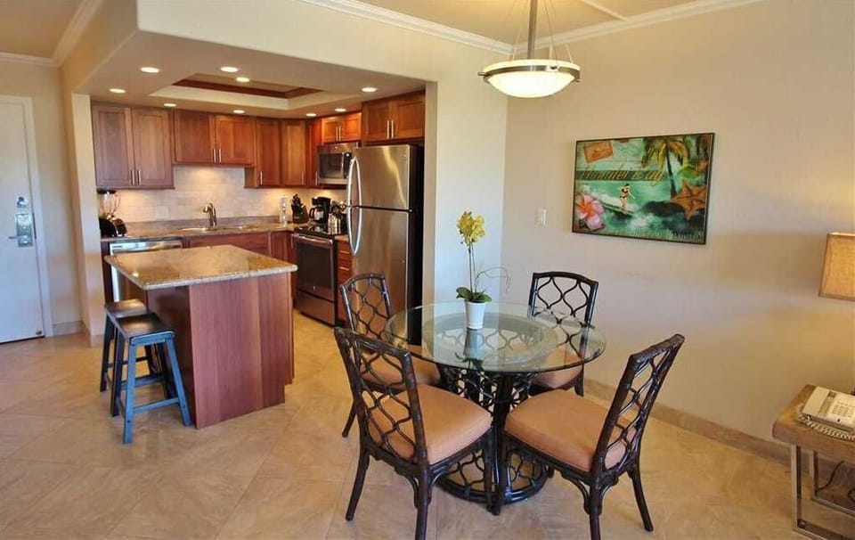 Your open-concept living space blends warm wood tones with elegant island seating and an intimate glass dining table—perfect for easy mornings or gathering with loved ones after a day exploring the island.