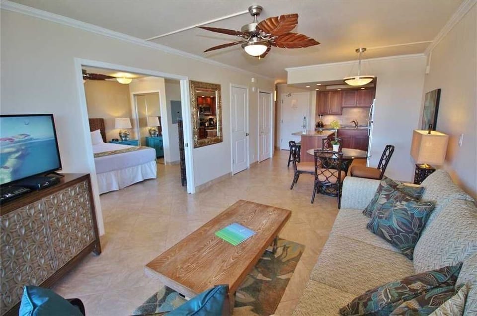 Picture yourself relaxing in this bright, open-concept space where living, dining, and kitchen flow seamlessly together. The tropical-themed décor and tile floors set a vacation vibe, while the leafed ceiling fan adds a soothing breeze.