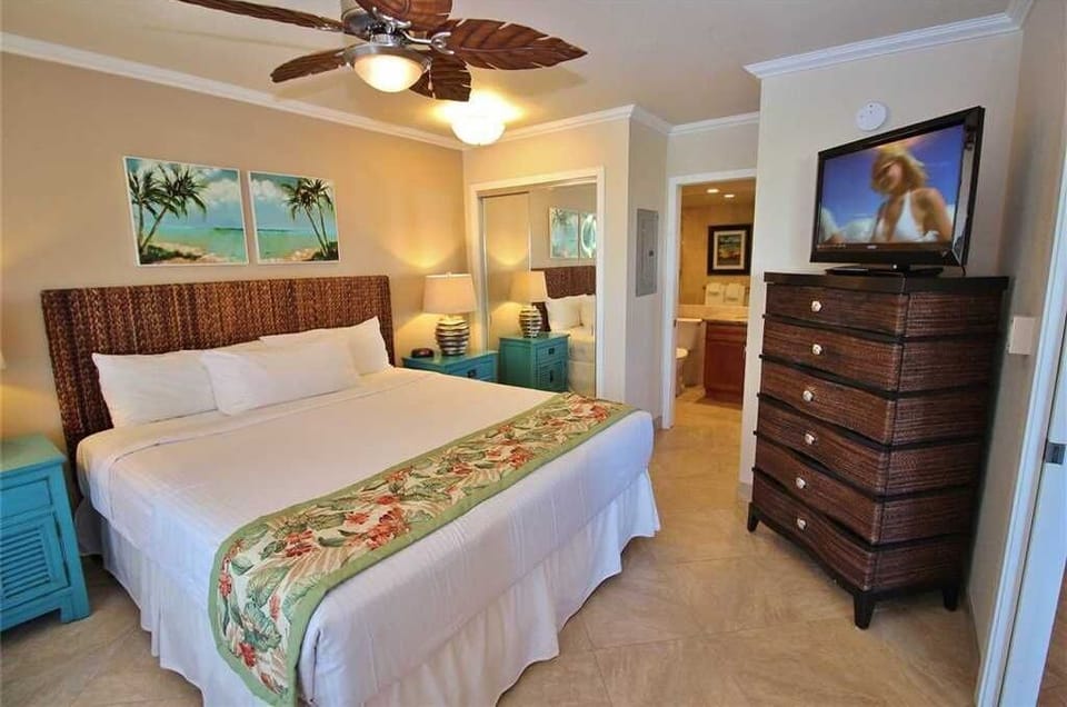 Your cozy bedroom retreat features a plush bed with tropical decor, ceiling fan, flat-screen TV, and stylish furnishings, creating the perfect space to unwind after a day of adventure.