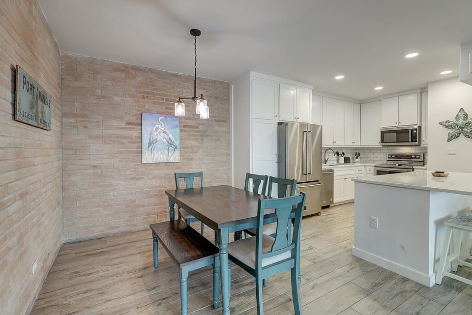 Your open-concept kitchen flows seamlessly into the dining area, featuring white cabinetry and a charming blue farmhouse table perfect for meals.