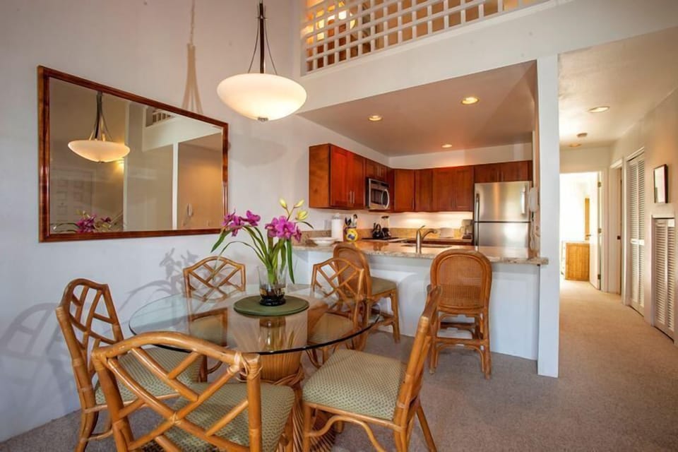 Your bright, airy space flows from dining to a fully equipped kitchen, with tropical touches like fresh orchids welcoming you. Notice the high ceilings and warm island-style details throughout.