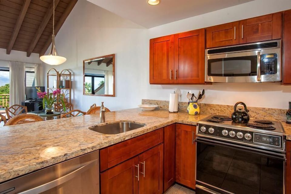 Step into your open-concept kitchen, where rich wood cabinetry, granite counters, and stainless appliances invite you to prepare island-inspired meals. Vaulted ceilings and natural light create a warm, welcoming space.