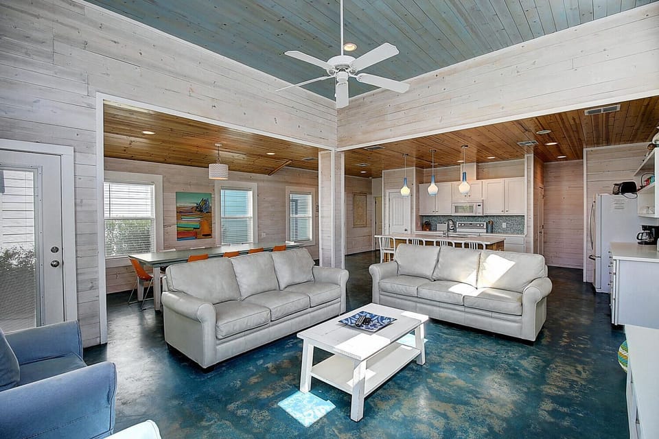 Relax in this stunning open-concept space where rustic wood meets coastal charm. Two plush gray sofas invite you to unwind while the kitchen beckons for culinary adventures.