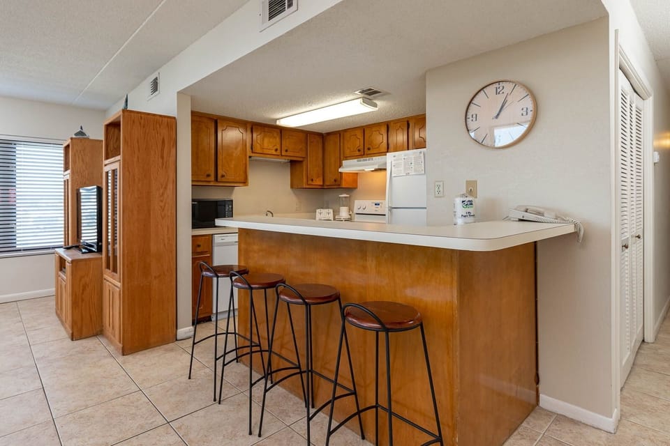 The kitchen features wooden cabinetry, white appliances, and a breakfast bar perfect for casual dining
