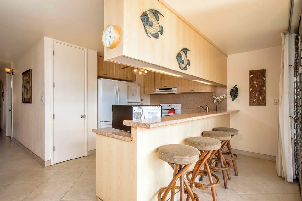 A bright open kitchen with breakfast bar seating invites you to gather for casual meals and morning coffee in this light-filled tropical retreat.