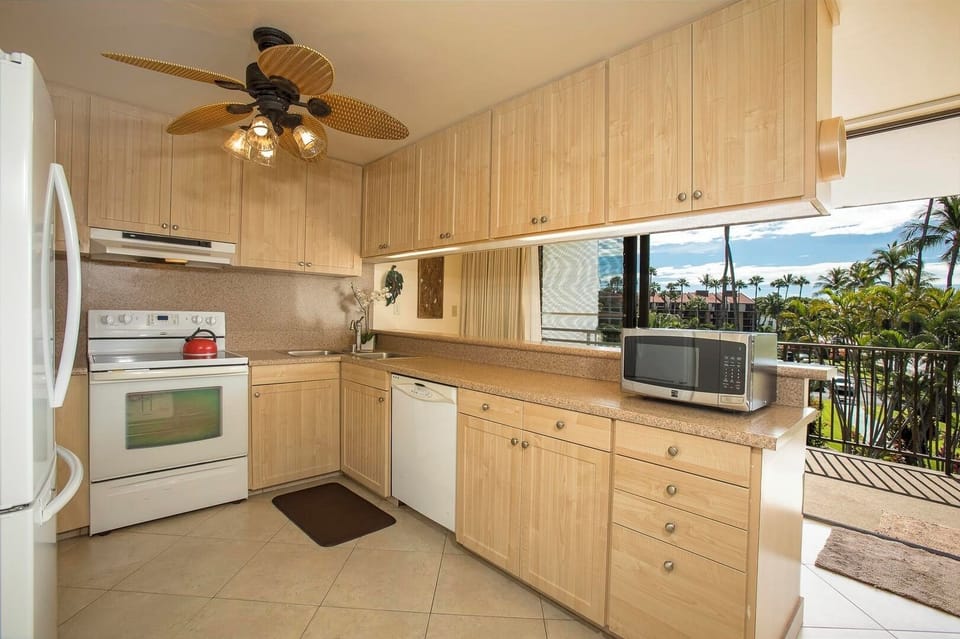 Prepare meals in your fully equipped kitchen with tropical views. Light wood cabinetry and modern appliances create a warm, inviting space that opens to the balcony.