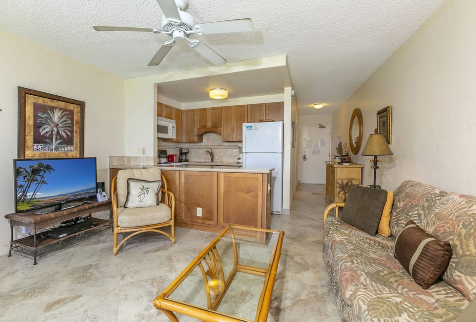 Relax in your open-concept living area with tropical-themed décor, ceiling fan, full kitchen, and flat-screen TV—perfect for unwinding after a day exploring the island.