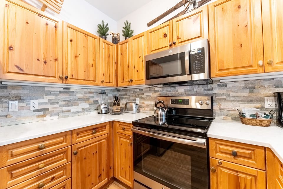 Cook your favorite meals in this fully-equipped kitchen featuring warm knotty pine cabinets, stone backsplash, and modern appliances for your comfort.
