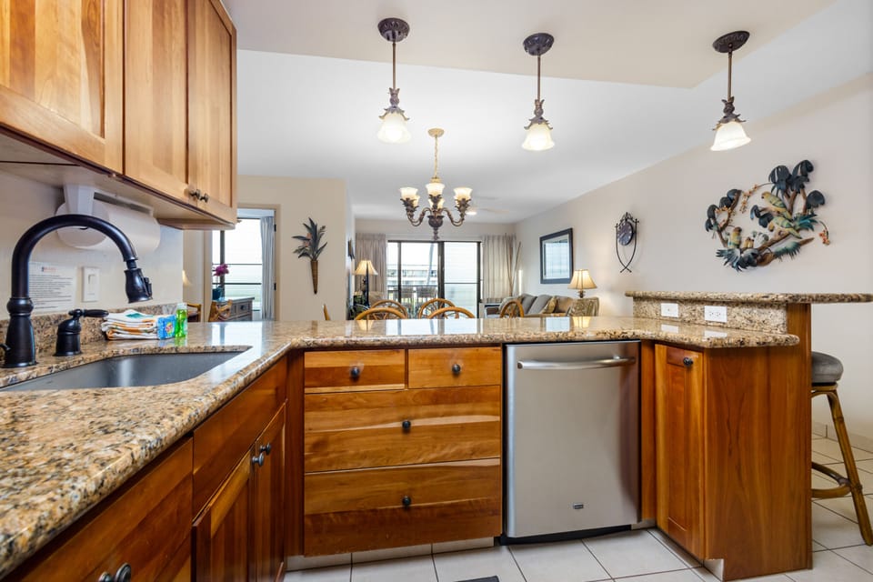 Your fully-equipped kitchen features granite counters, modern appliances, and plenty of space to prepare meals with natural light streaming in from the open living area beyond.