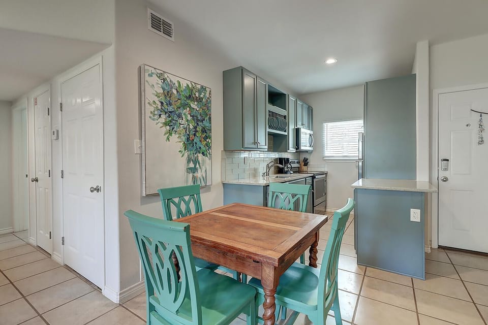 Your bright dining area flows seamlessly into the modern kitchen, where turquoise chairs and cheerful artwork create a welcoming coastal vibe.