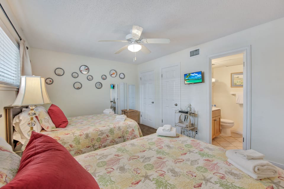 Your cozy twin bedroom features coastal charm with decorative plates, ceiling fan, and en-suite bathroom for restful nights.