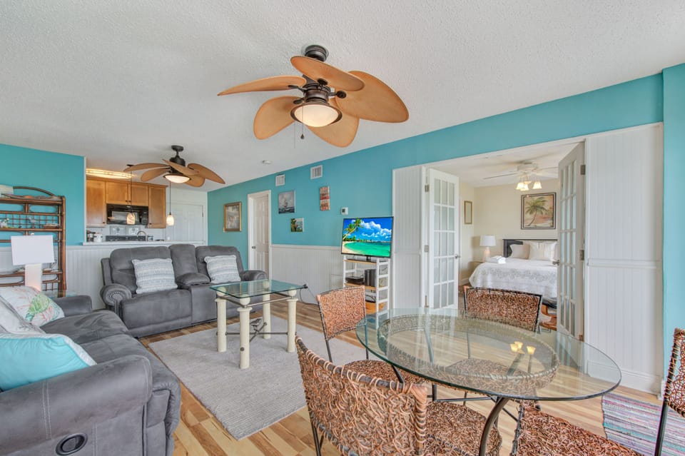 Your coastal retreat features vibrant turquoise walls and comfy gray recliners perfect for unwinding after beach days.
