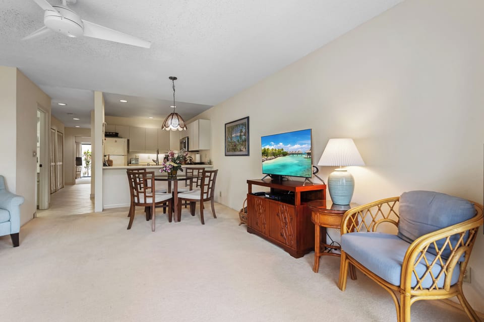 Settle into your bright, open living and dining area where soft seating, tropical artwork, and a ceiling fan welcome you to unwind—your kitchen just steps away.