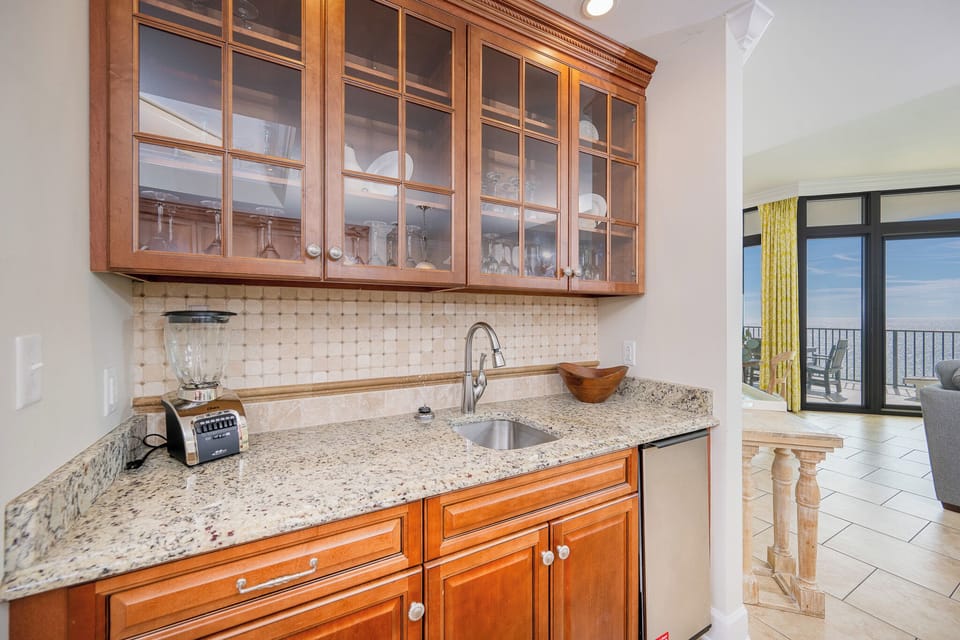 Enjoy a well-appointed wet bar with rich wooden cabinetry, granite countertops, and a view of the inviting living area