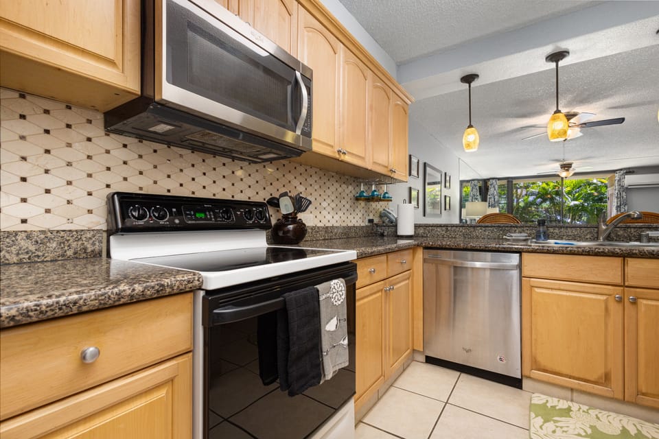 Your fully equipped kitchen features modern appliances and granite countertops, perfect for preparing meals during your stay. Natural light streams in from the living area, creating a warm and inviting space.