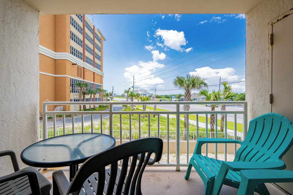 Enjoy a relaxing moment on the balcony with vibrant turquoise chairs and a view of swaying palm trees and blue skies