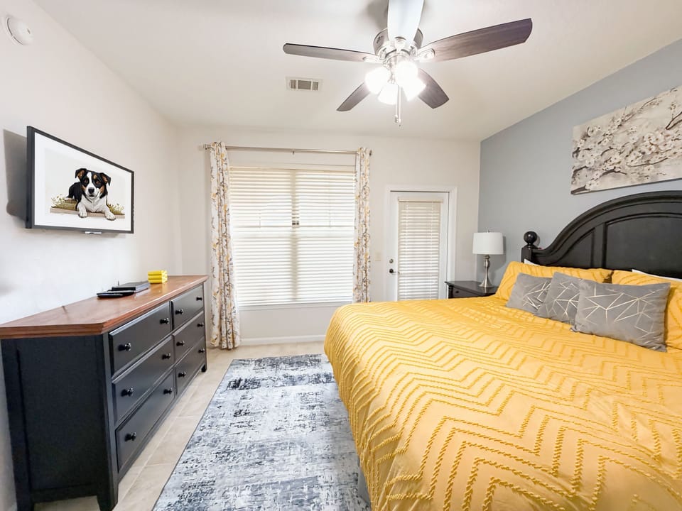 Spacious king bedroom with yellow bedding, ceiling fan, and private outdoor access in an Orlando vacation rental near Disney.