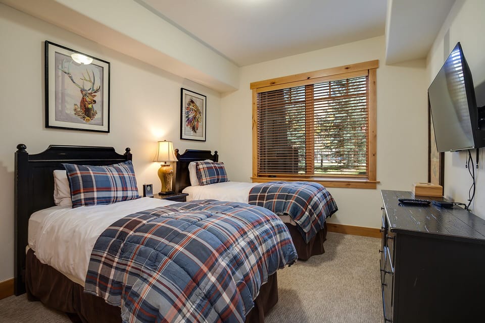 Your cozy twin bedroom features plaid bedding and warm lighting, perfect for restful nights after mountain adventures.