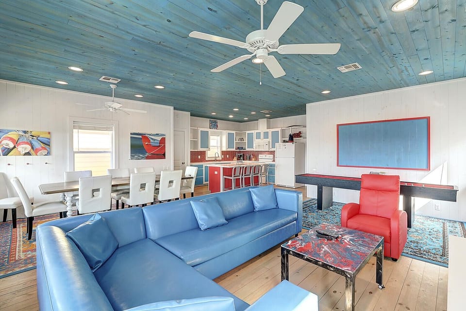 Relax in your vibrant open-plan retreat featuring a stunning blue leather sectional, pool table, and coastal-inspired decor under charming reclaimed wood ceilings.