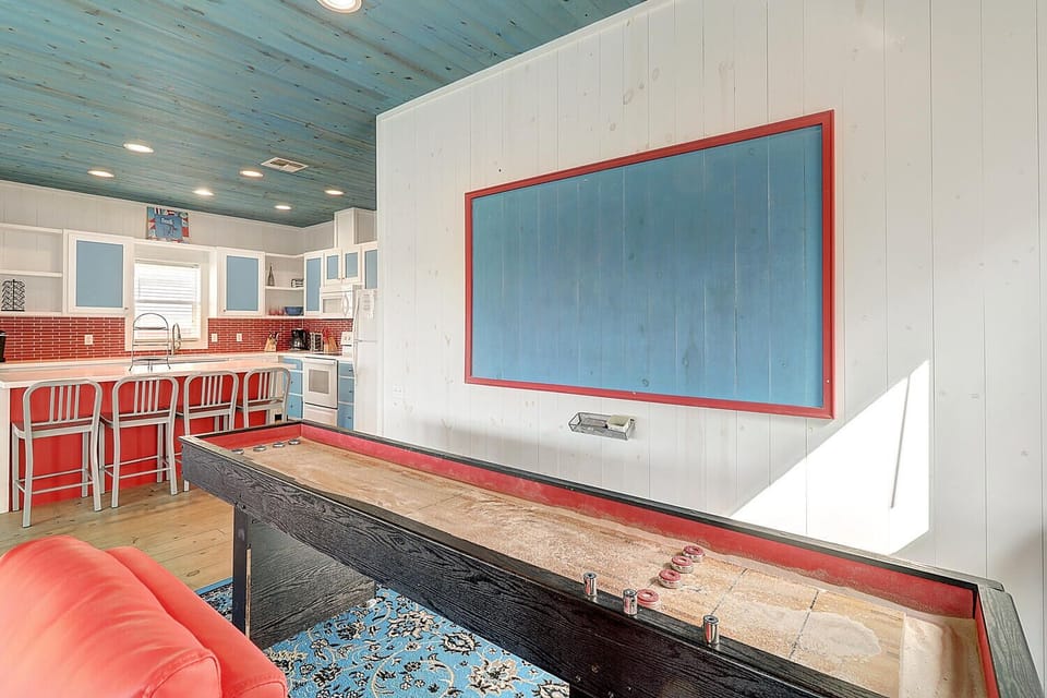 Challenge your friends to shuffleboard in this vibrant game room, featuring colorful coastal decor and modern kitchen access for snacks.
