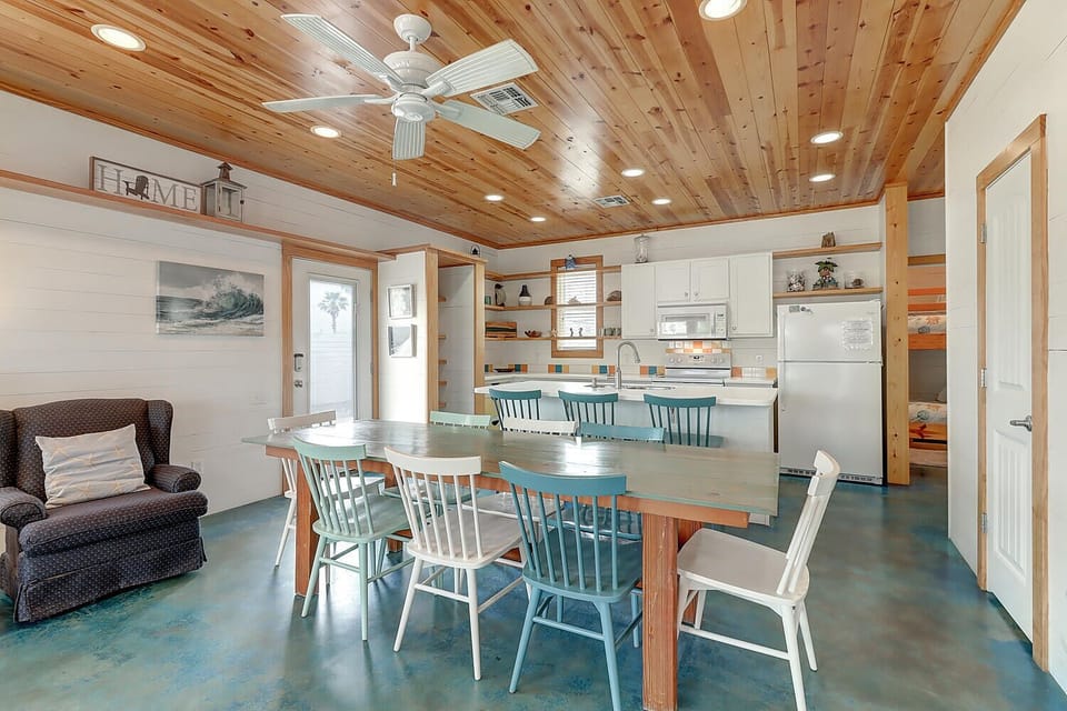 Gather around the handcrafted dining table beneath soaring wood ceilings, where coastal charm meets modern comfort in your open-concept retreat.