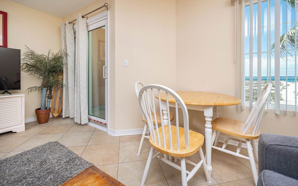 This cozy dining area features a round wooden table, a TV, and a stunning beach view through large windows