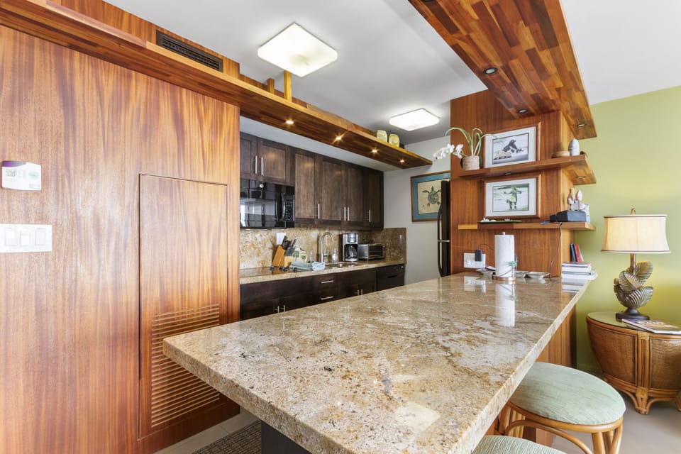 Picture yourself preparing meals on gleaming granite countertops in this tropical-inspired kitchen. Modern appliances and warm wood cabinetry create an inviting space where your vacation culinary adventures begin.