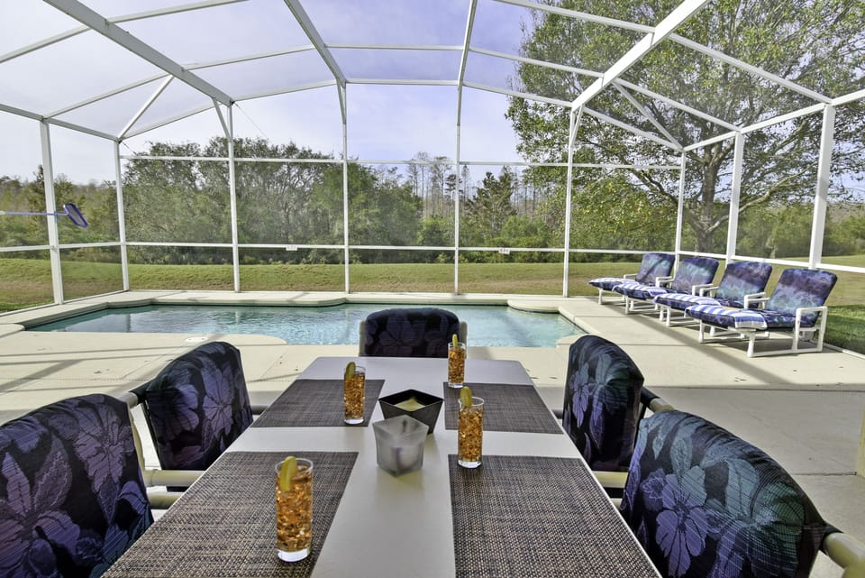 Covered outside dining table with seating for six and screened pool view.