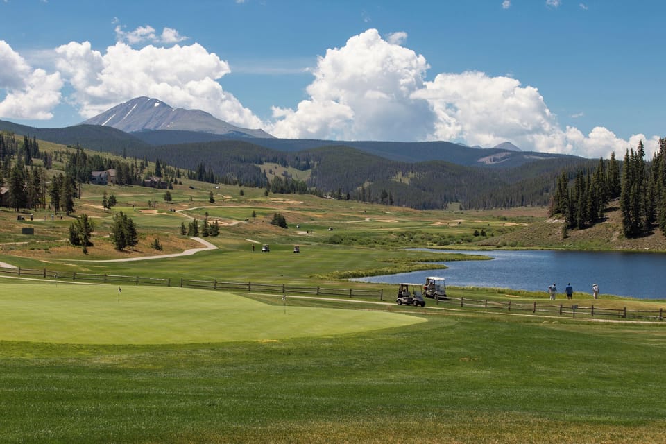 Championship golf course set against majestic mountain peaks, with pristine fairways winding around a serene alpine lake.