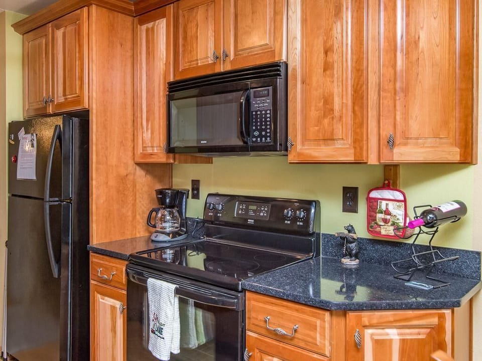 Black appliances, including microwave and stove, contrast with honey-toned wood cabinetry and dark granite countertops.
