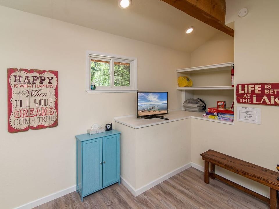 Small entertainment nook with flat-screen TV on white shelf, light wood flooring, and rustic wooden bench beneath wall shelves.