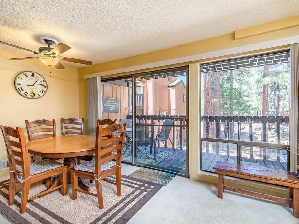 Wooden dining table with six carved chairs, ceiling fan overhead, and sliding glass doors to a balcony with forest views.