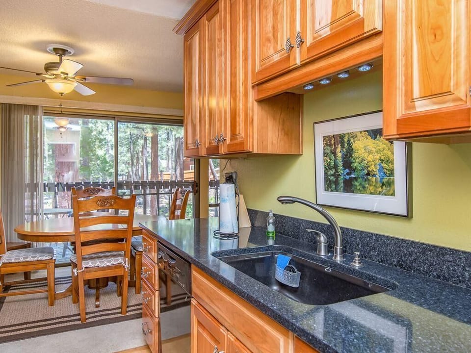 Black granite countertops and honey-toned cabinetry line the kitchen, adjacent to a wooden dining table with carved chairs.