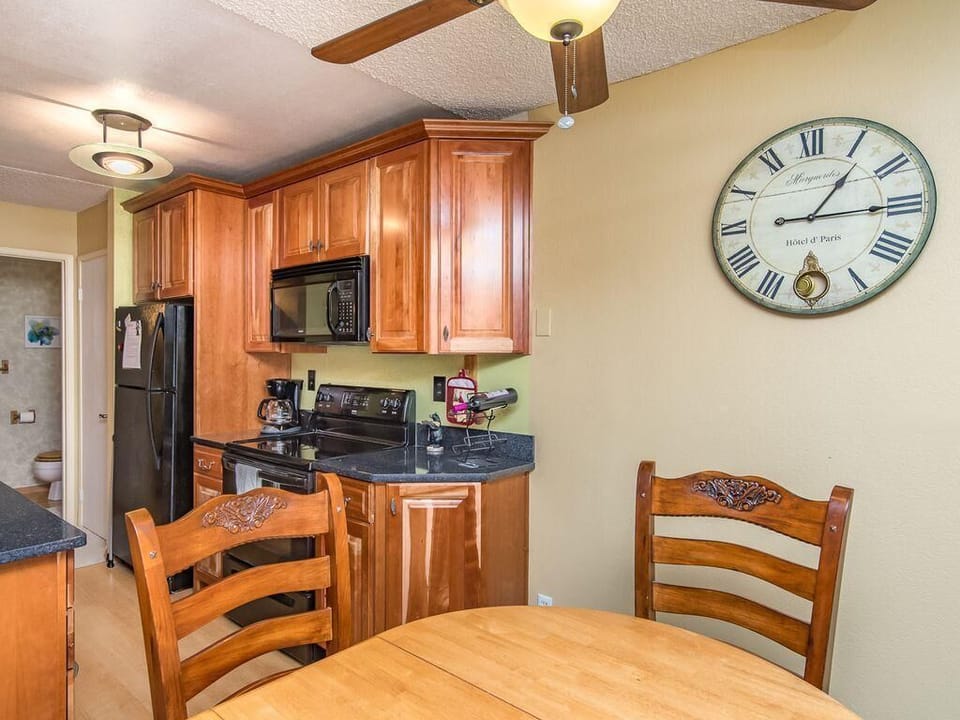 Kitchen and dining nook with honey-toned cabinetry, black appliances, granite countertops, and a round wooden table.