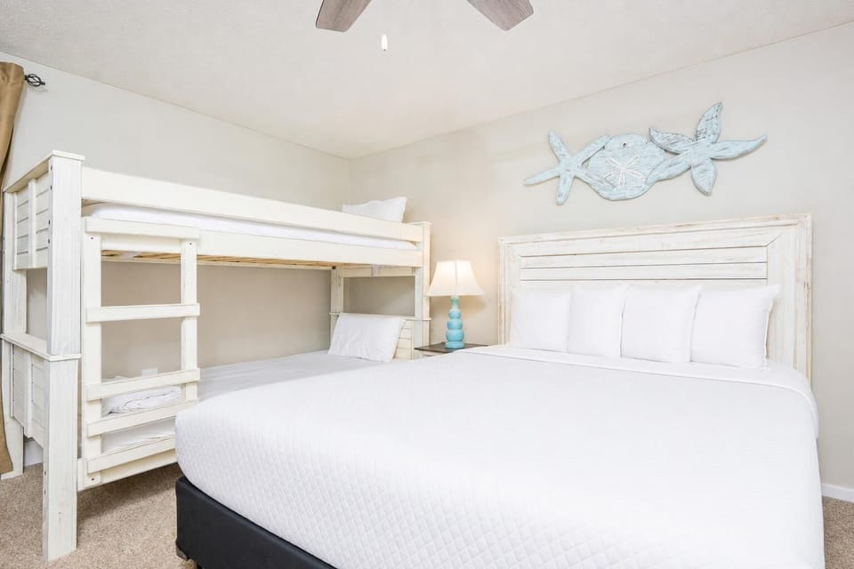 This cozy bedroom features a charming twin bunk bed and a queen bed, accented by beach-themed decor and soft lighting