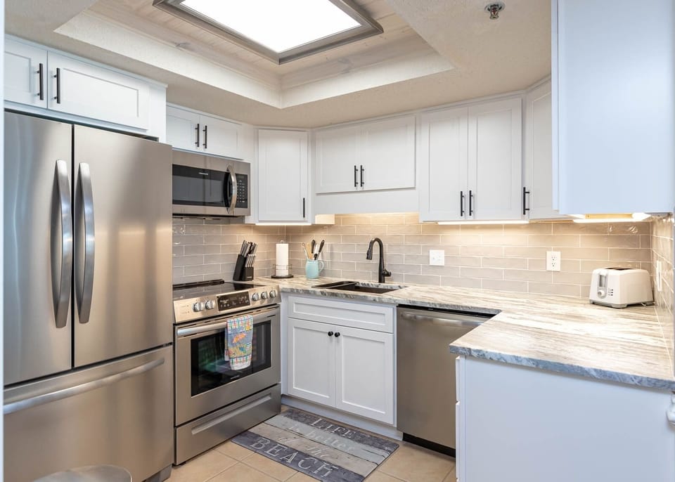 The kitchen features sleek stainless appliances, elegant granite countertops, and a beach rug for a delightful experience