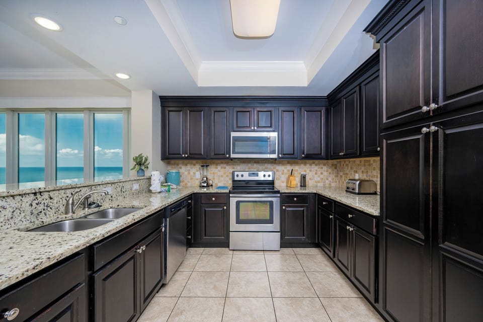 Prepare meals in the stylish kitchen featuring dark cabinetry, granite countertops, and expansive views of the beach