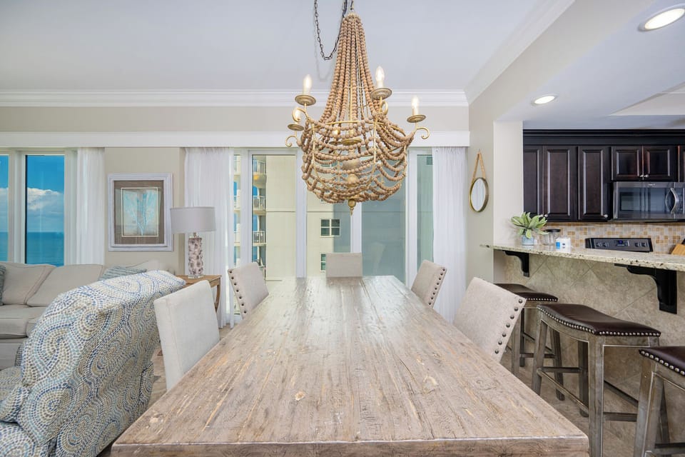 Gather around the rustic dining table under a unique chandelier, with views of the beach through large windows