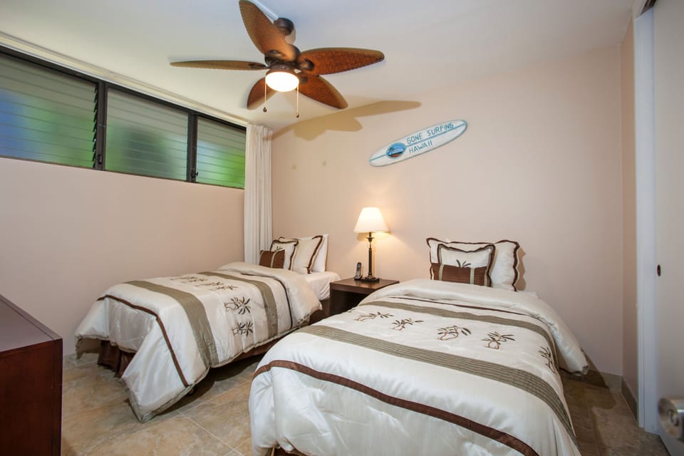 Your island-themed bedroom features two comfortable twin beds dressed in tropical linens, a ceiling fan to keep you cool, and charming surf-inspired décor that sets a relaxing vacation mood.