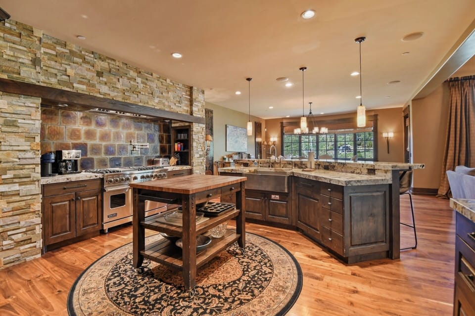 Imagine cooking here: a chef-worthy kitchen with a grand stone-clad range hood, professional-grade appliances, granite counters, and warm wood floors—your home away from home.