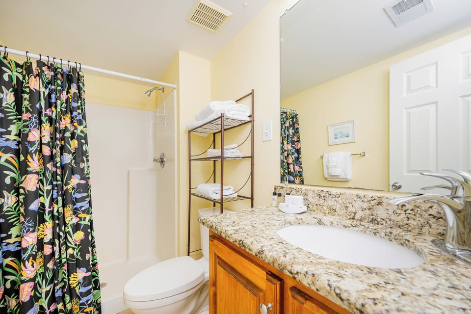 Soft yellow walls surround the master bath where you refresh beneath the colorful aquatic shower curtain