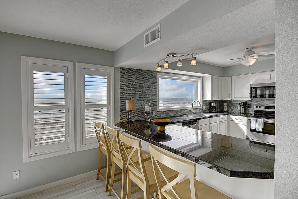 Your sleek kitchen features granite counters, modern appliances, and panoramic ocean views through plantation shutters - perfect for morning coffee.