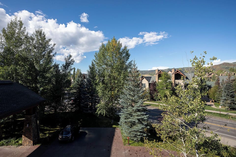 Tree-lined neighborhood with mountain views beneath blue skies and fluffy white clouds.
