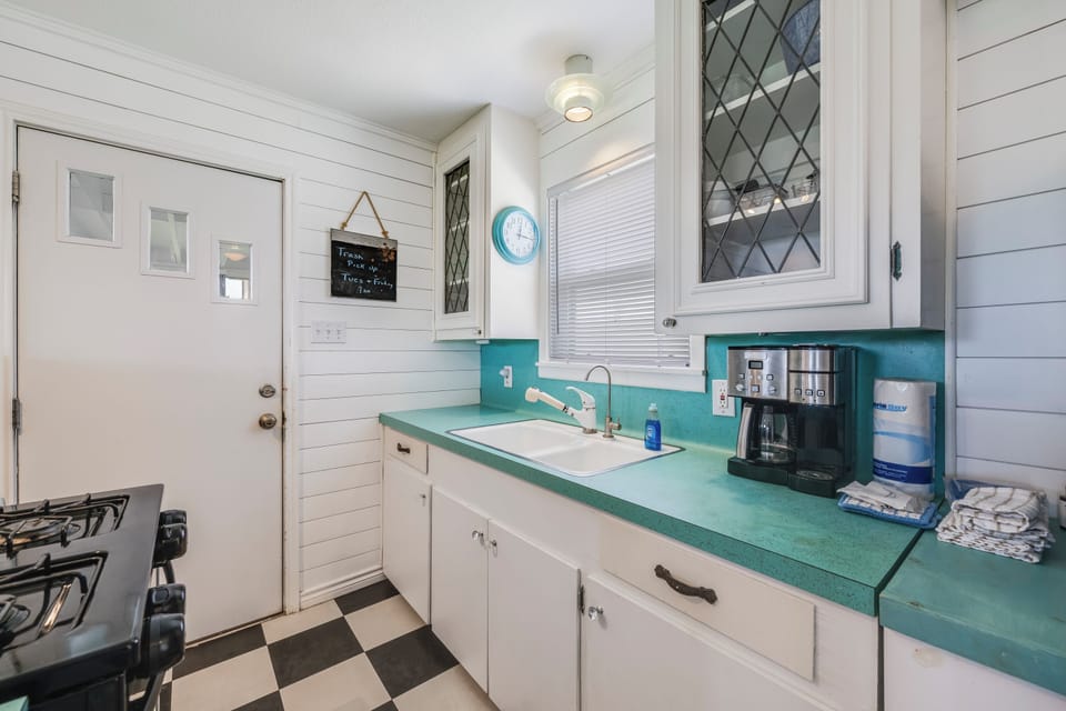 Your bright, retro-style kitchen features turquoise countertops, white shiplap walls, and checkered floors. Everything you need—coffee maker, full-sized stove, and cozy charm—awaits your morning routine.