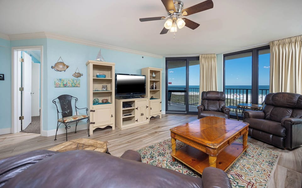 Cozy living area features leather recliners, a wooden coffee table, and expansive views of the beach through large windows