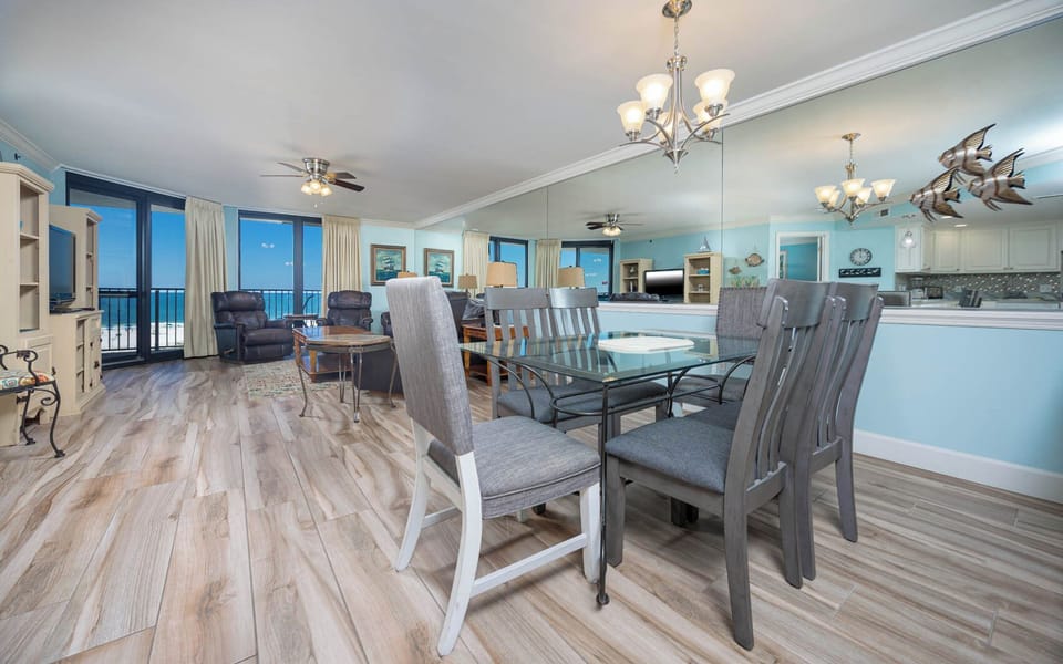 Bright dining area features a glass table surrounded by stylish chairs, with views of the beach visible through large windows