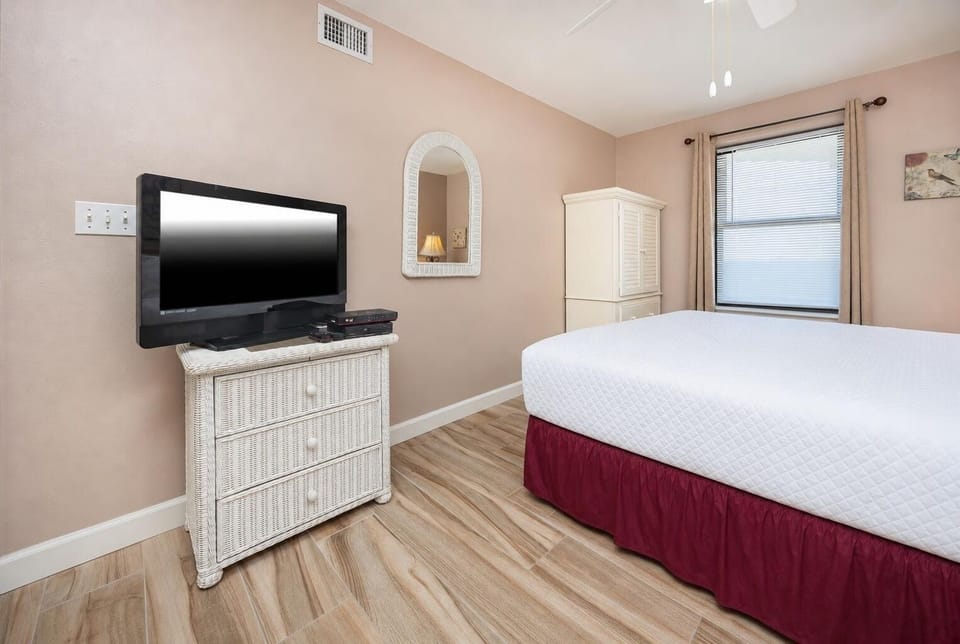 Guest room featuring a queen bed, a flat-screen TV on a wicker dresser, and a cozy atmosphere