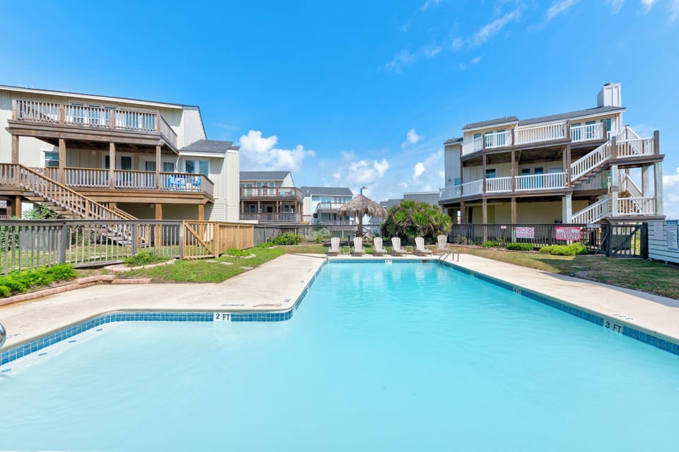 Dive into your private retreat—a sparkling community pool framed by coastal villas, sun loungers waiting, and ocean breezes just beyond the dunes.