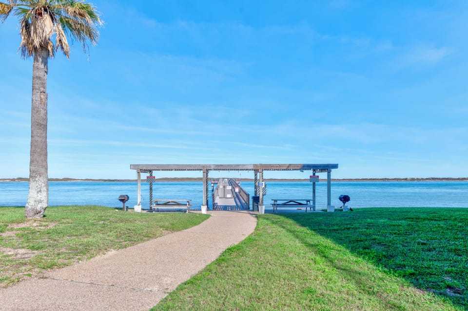 Waterfront pavilion with private dock access overlooking tranquil bay waters, surrounded by manicured lawns and tropical palms.