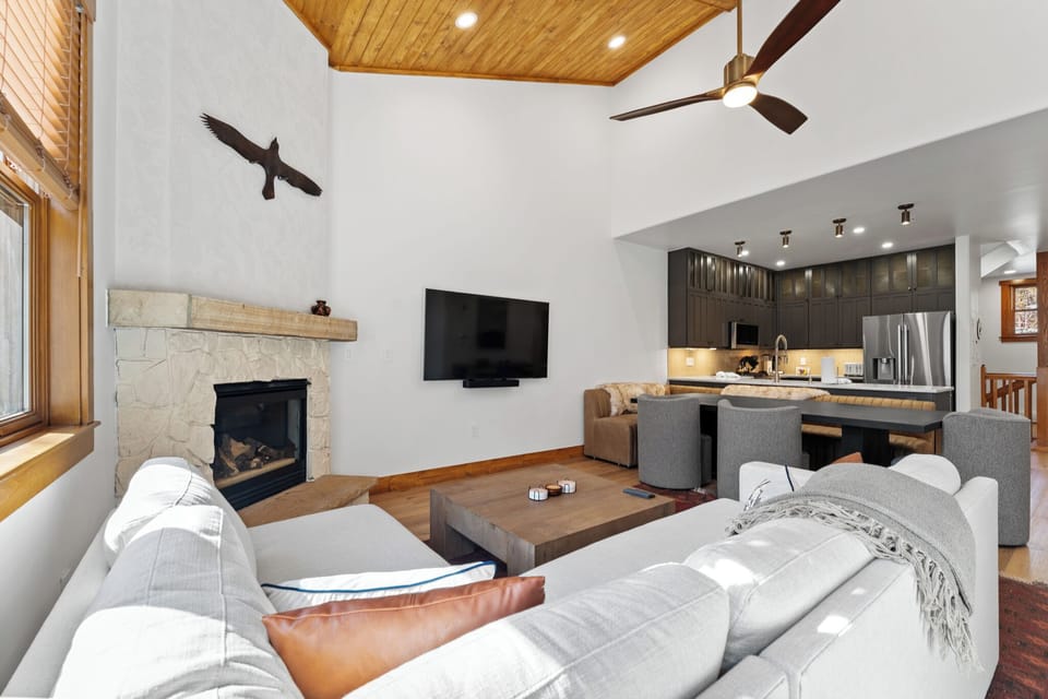 Relax in your open-concept living space featuring a cozy stone fireplace, modern kitchen, and comfortable seating perfect for mountain evenings.